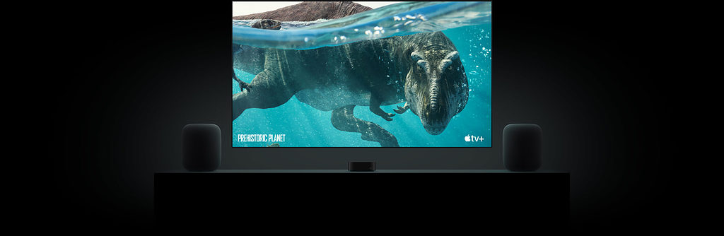 Two HomePods askance a television showing a T-Rex swimming. 
