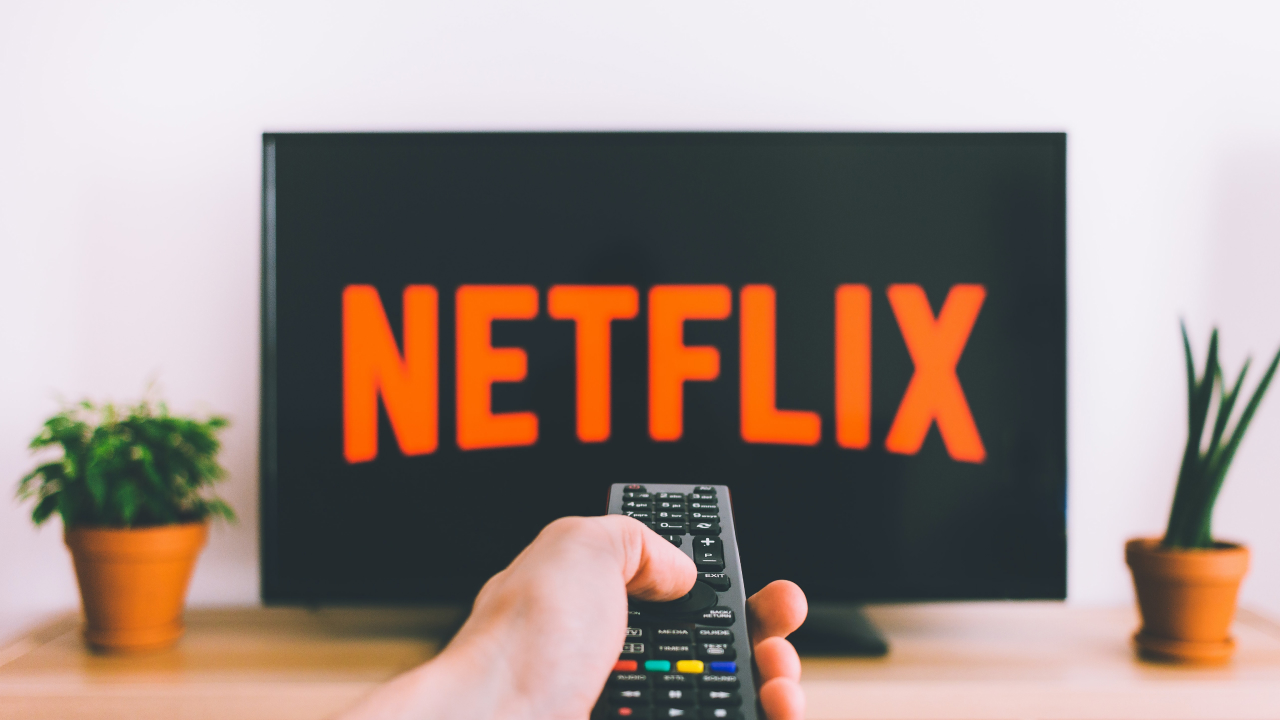 Hand pointing remote at television showing Netflix logo.